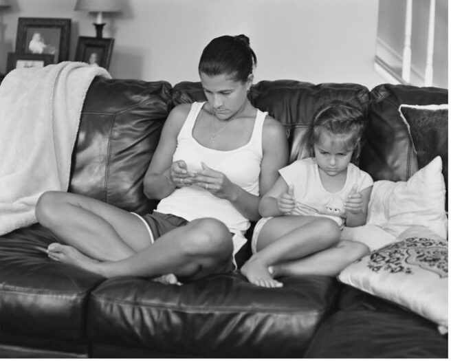 Black and White Image of a Mother and Daughter sitting on a couch looking at their imaginary phones